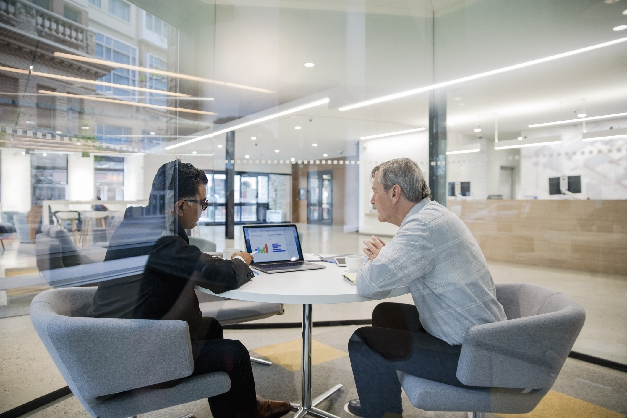 2 people at a table together in an office, pointing at a graph on a computer screen