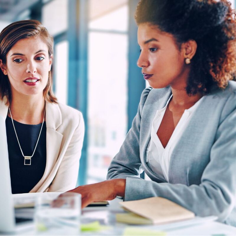 2 women looking at a laptop together in suits