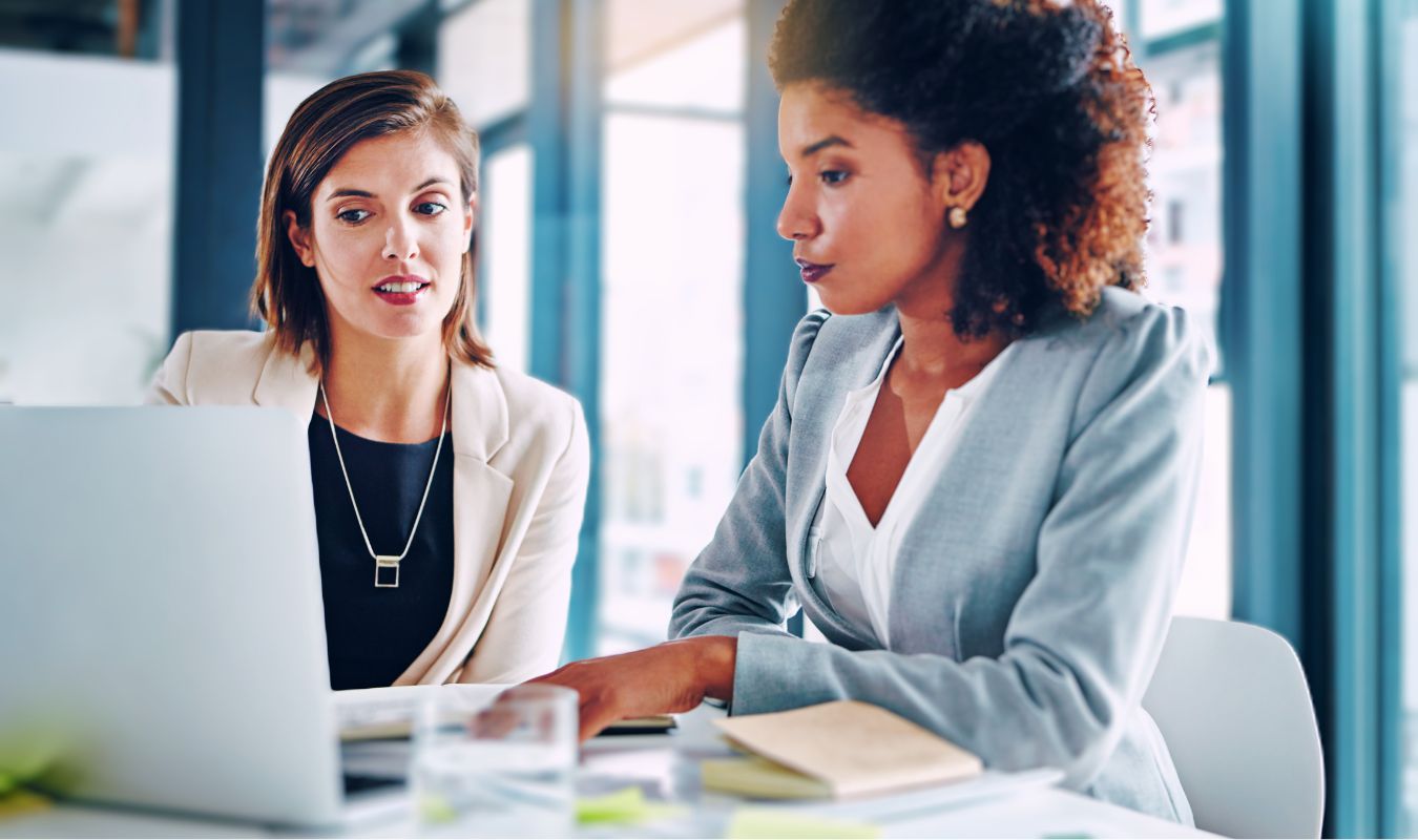 2 women looking at a laptop together in suits